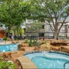 hot tub and pool with trees and rocks with a building behind it