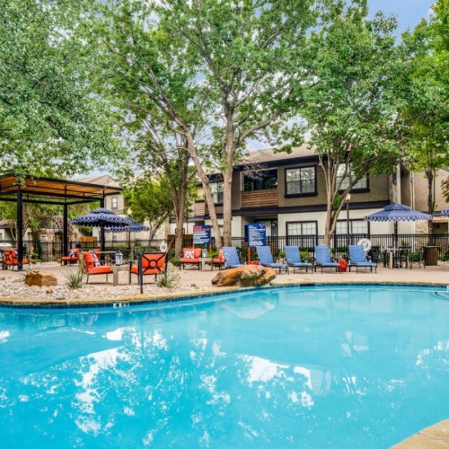 Relax and unwind poolside a swimming pool with trees and a building in the background